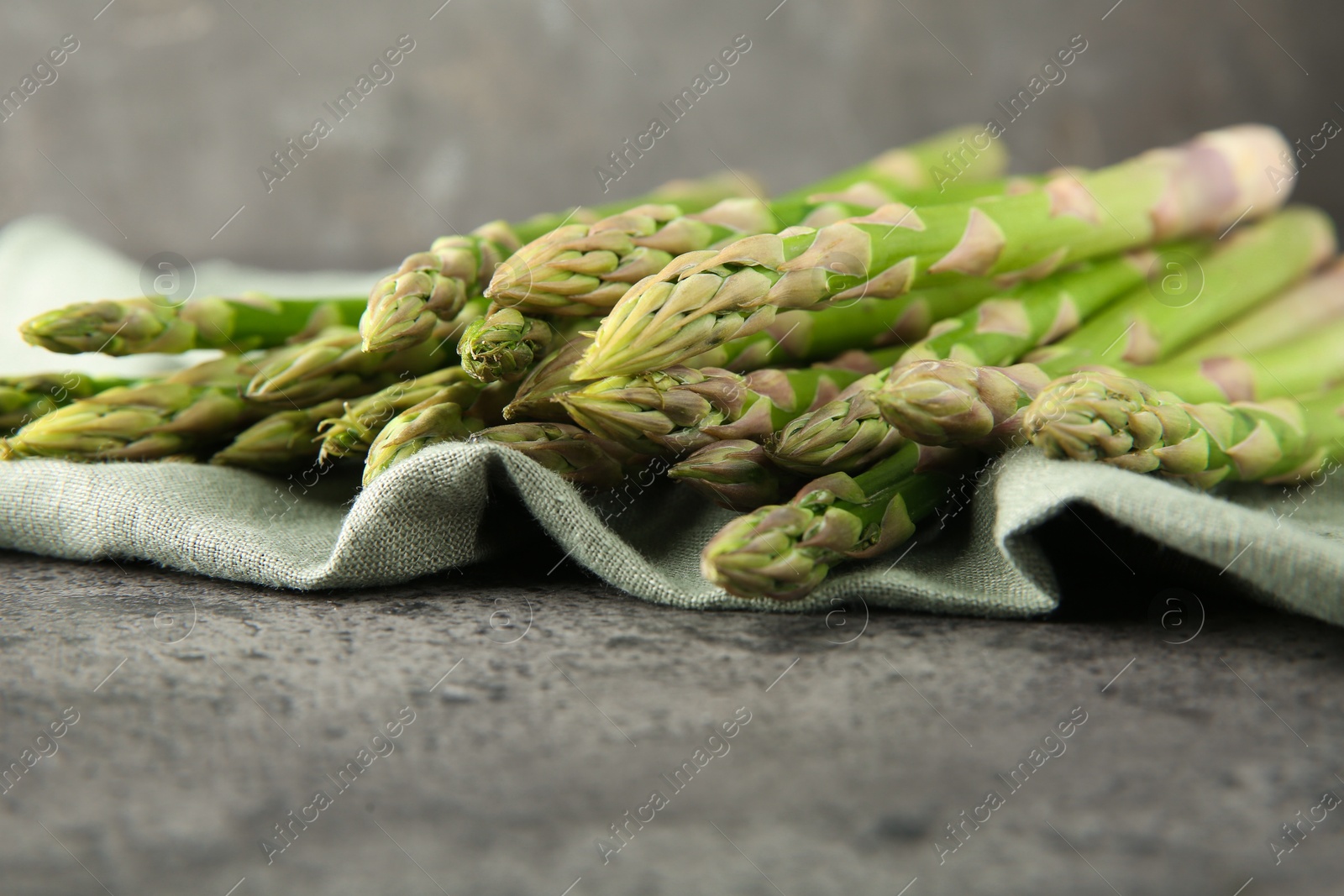 Photo of Fresh green asparagus stems on grey textured table, closeup