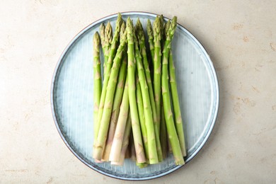 Plate with fresh green asparagus stems on light textured table, top view