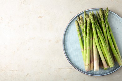 Photo of Plate with fresh green asparagus stems on light textured table, top view. Space for text