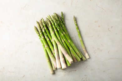 Many fresh green asparagus stems on light textured table, top view