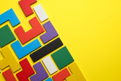 Colorful wooden puzzle pieces on yellow background, top view