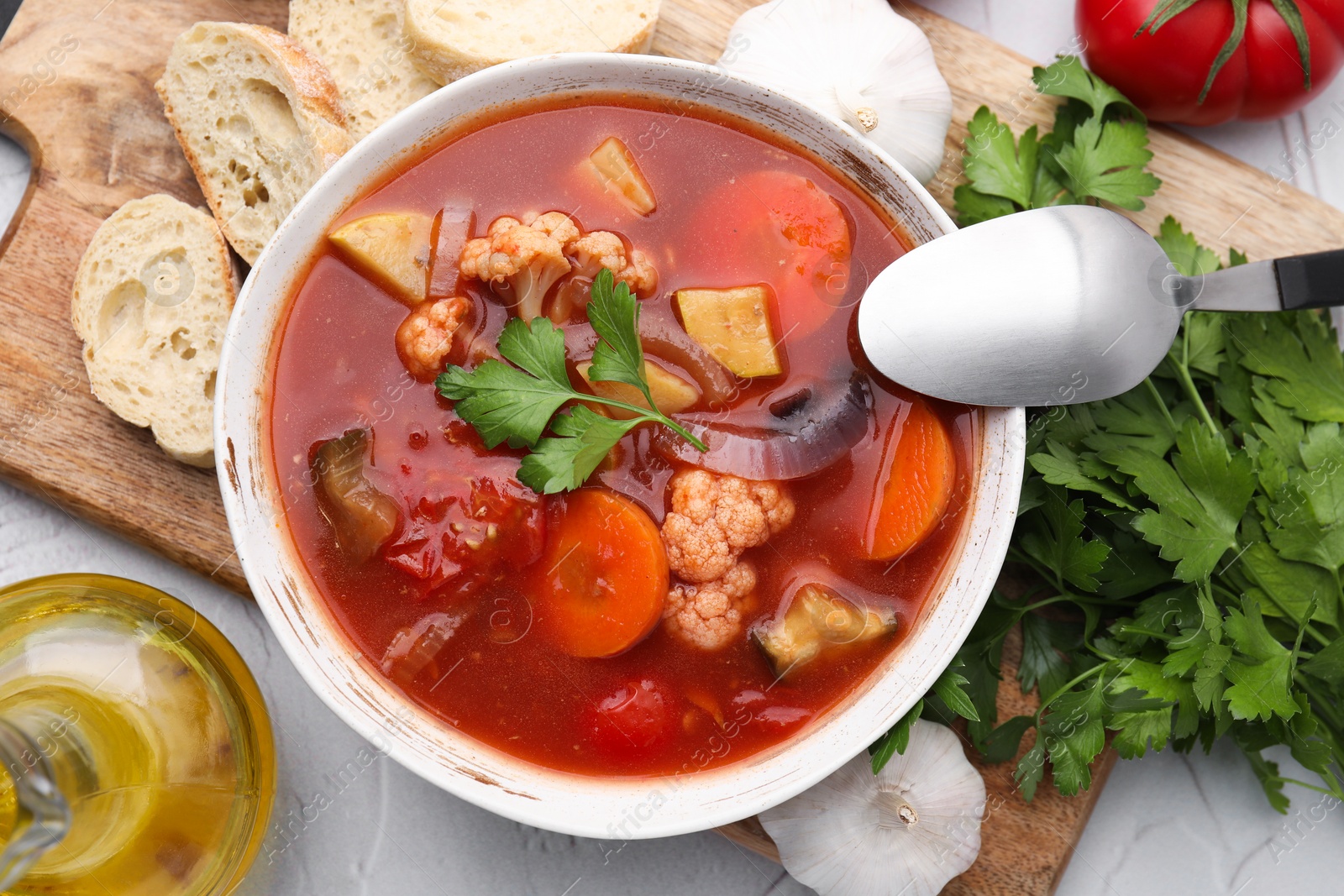 Photo of Delicious homemade stew in bowl, bread and parsley on light table, flat lay