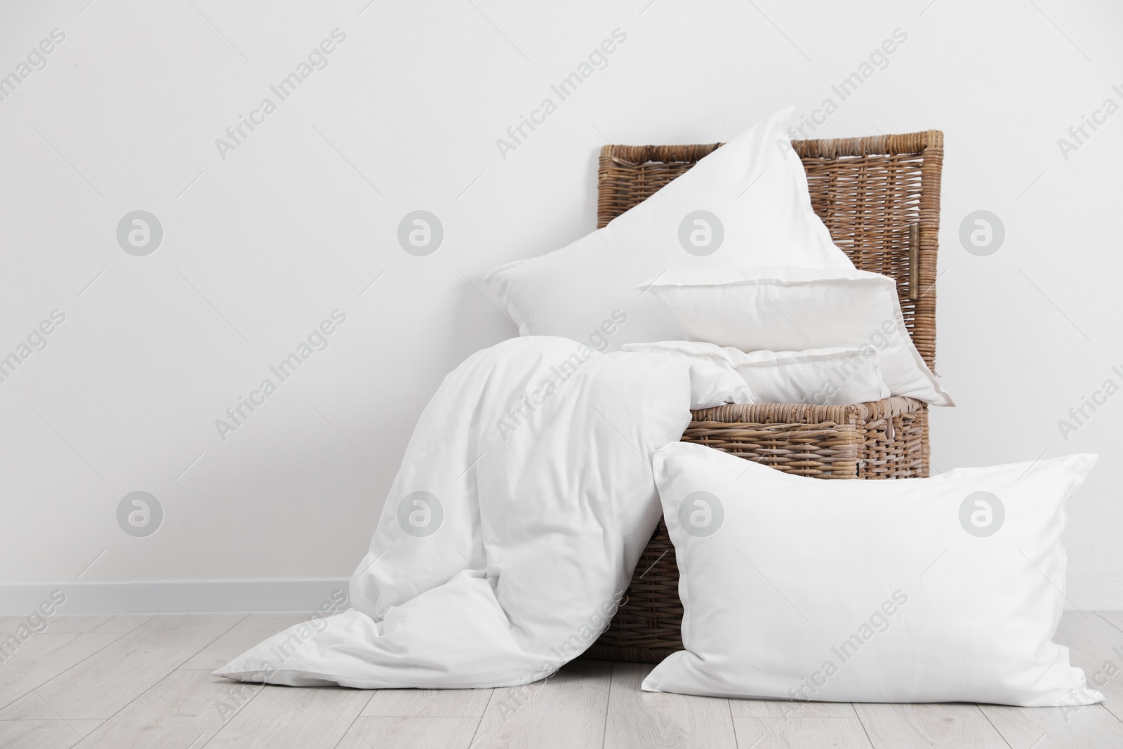 Photo of Clean pillows, duvet and storage basket on floor near white wall. Space for text