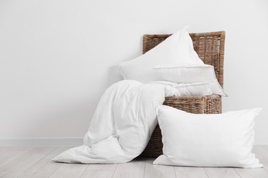 Clean pillows, duvet and storage basket on floor near white wall. Space for text