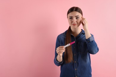 Photo of Confused woman holding pregnancy test on pink background, space for text