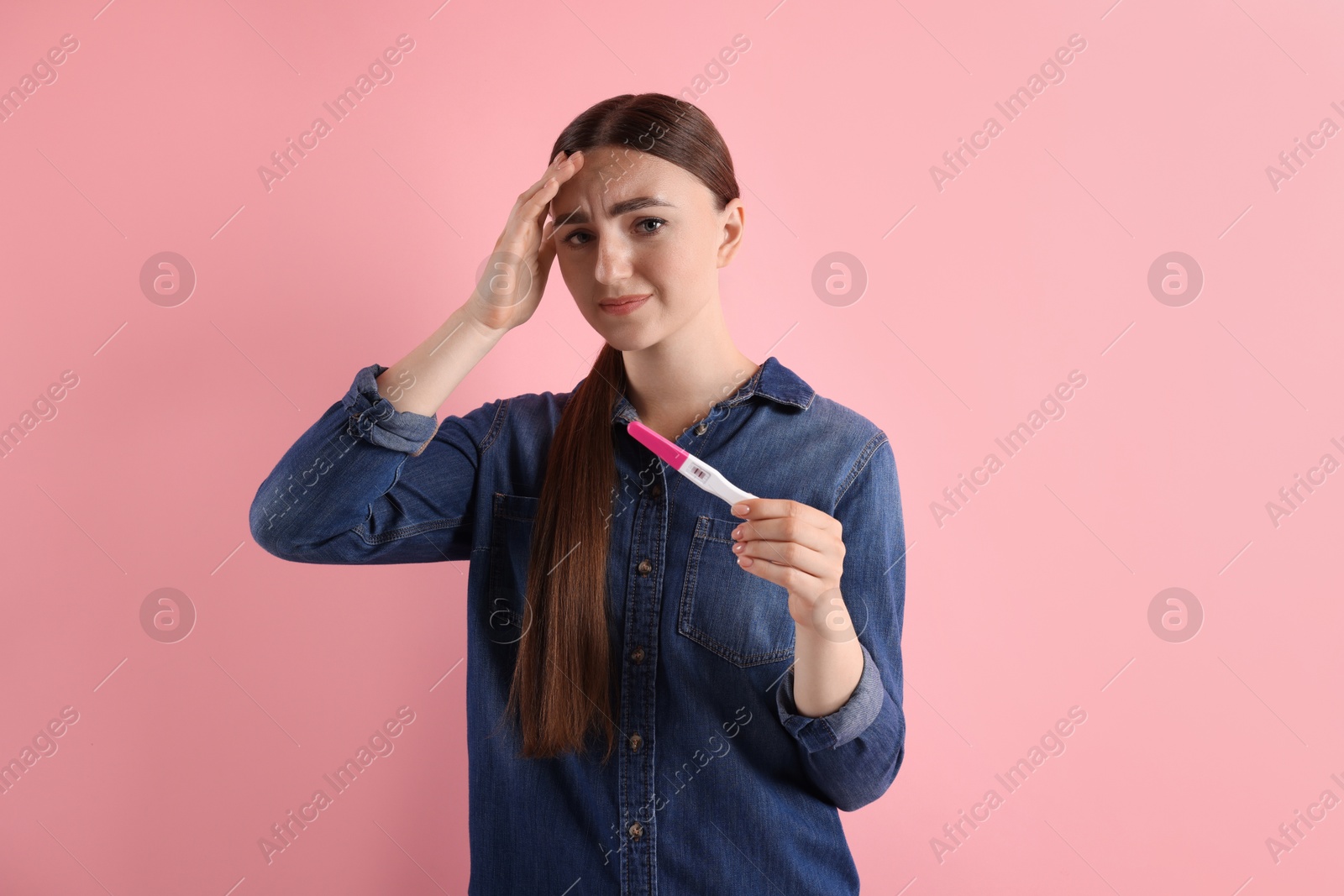 Photo of Confused woman holding pregnancy test on pink background