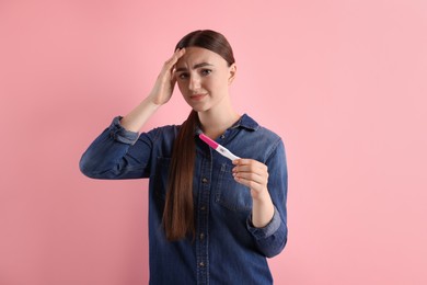 Confused woman holding pregnancy test on pink background