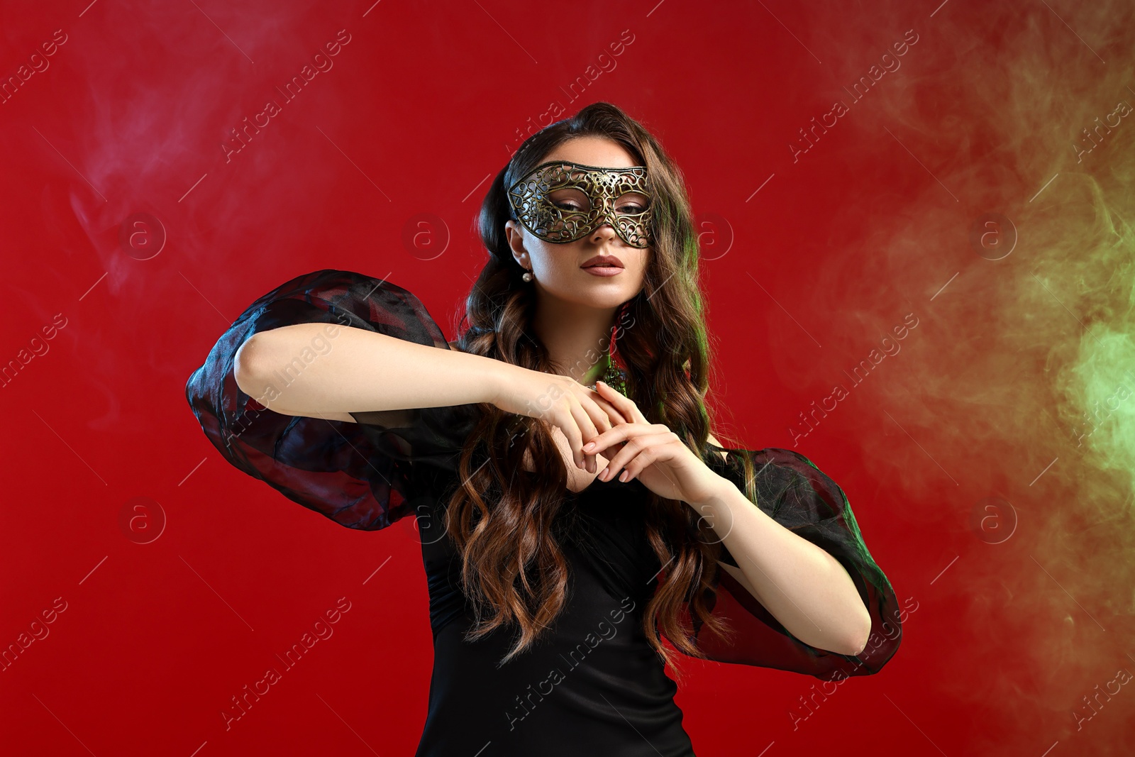 Photo of Beautiful woman wearing carnival mask on red background in color lights and smoke