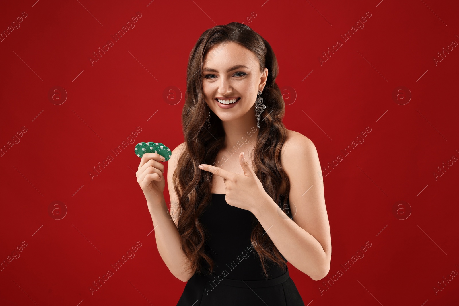 Photo of Smiling woman pointing at poker chips on red background