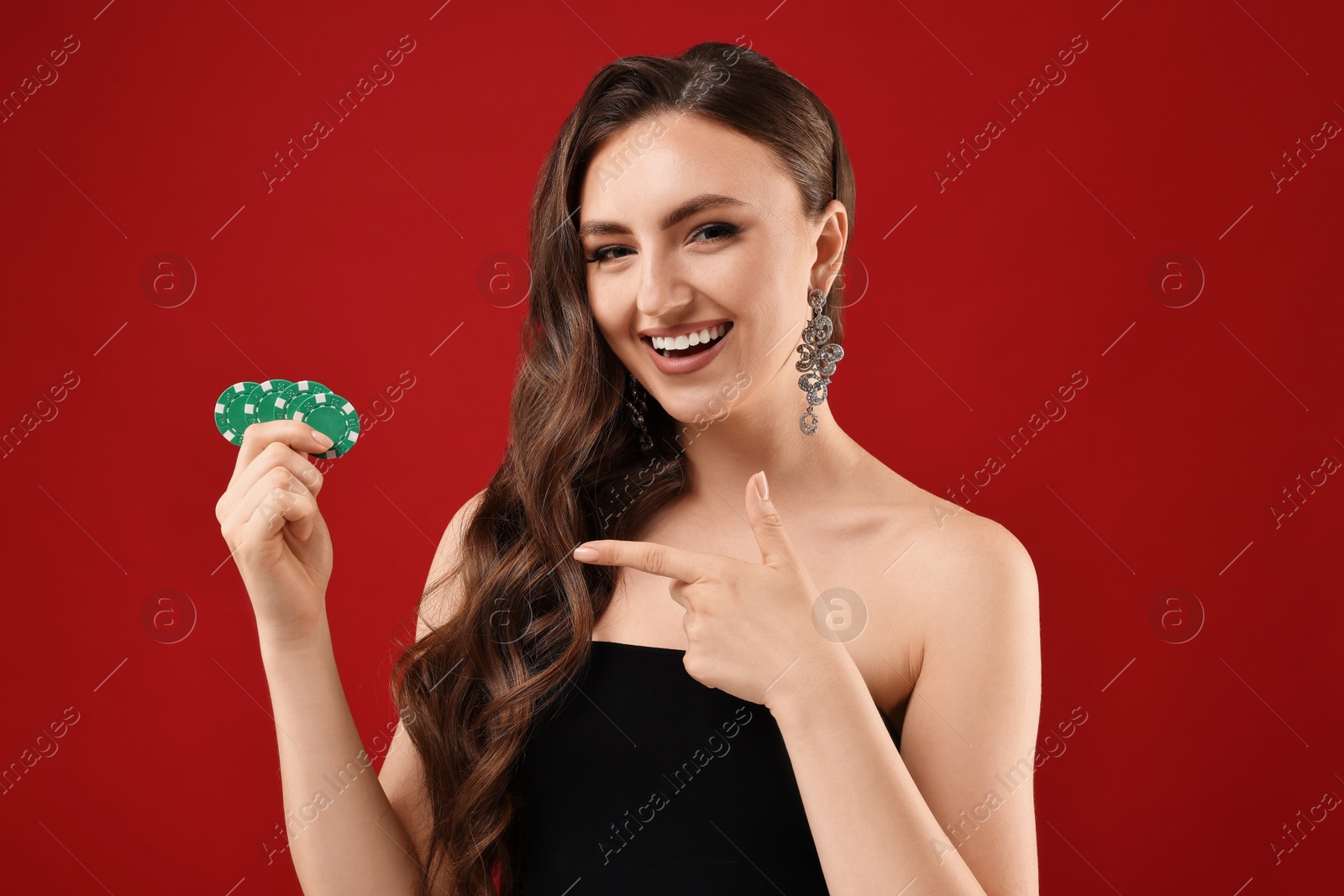 Photo of Smiling woman pointing at poker chips on red background