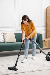 Photo of Young woman cleaning carpet with vacuum in living room