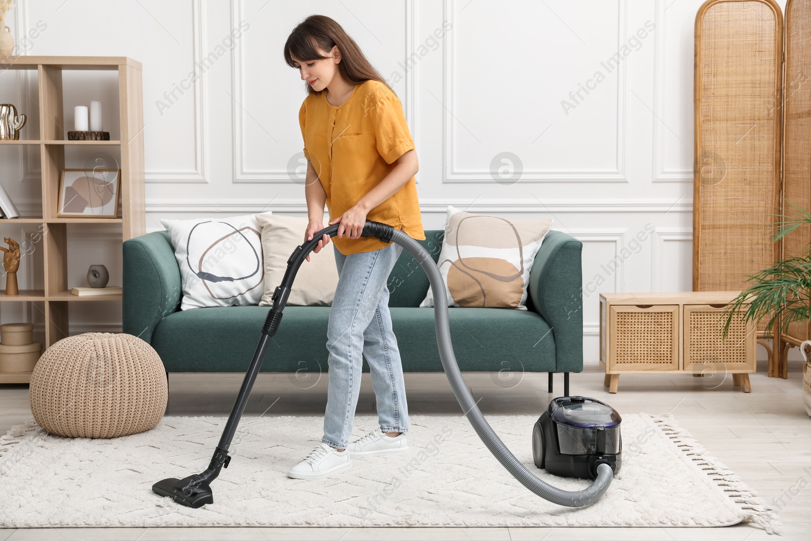 Photo of Young woman cleaning carpet with vacuum in living room