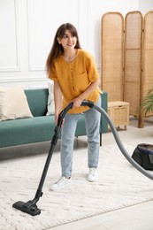 Photo of Young woman cleaning carpet with vacuum in living room