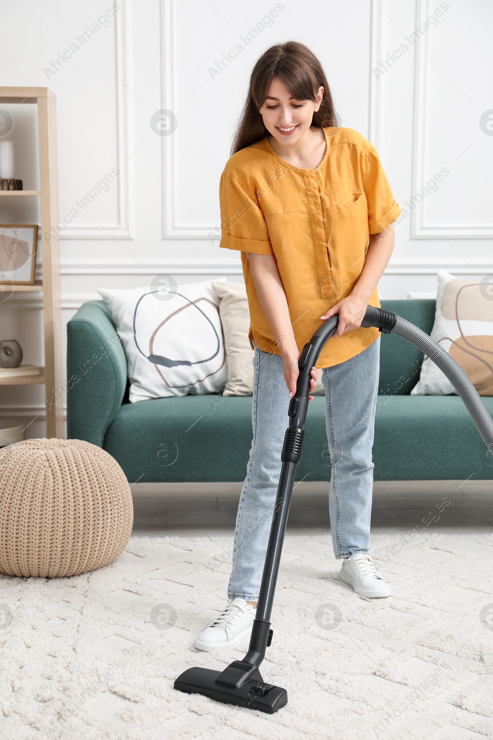 Photo of Young woman cleaning carpet with vacuum in living room