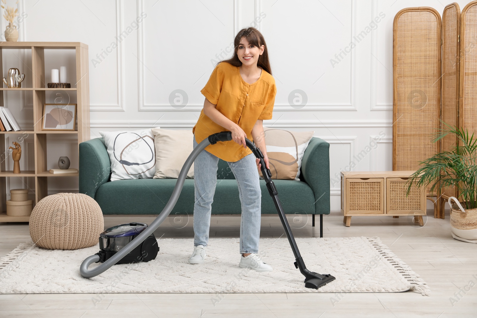 Photo of Young woman cleaning carpet with vacuum in living room