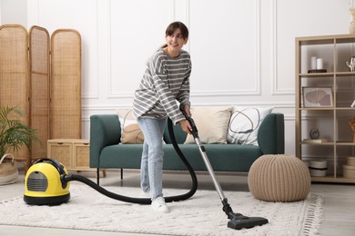 Photo of Young woman cleaning carpet with vacuum in living room