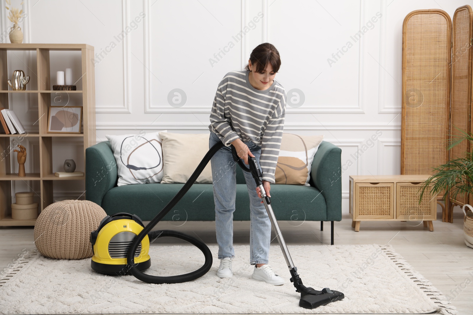 Photo of Young woman cleaning carpet with vacuum in living room