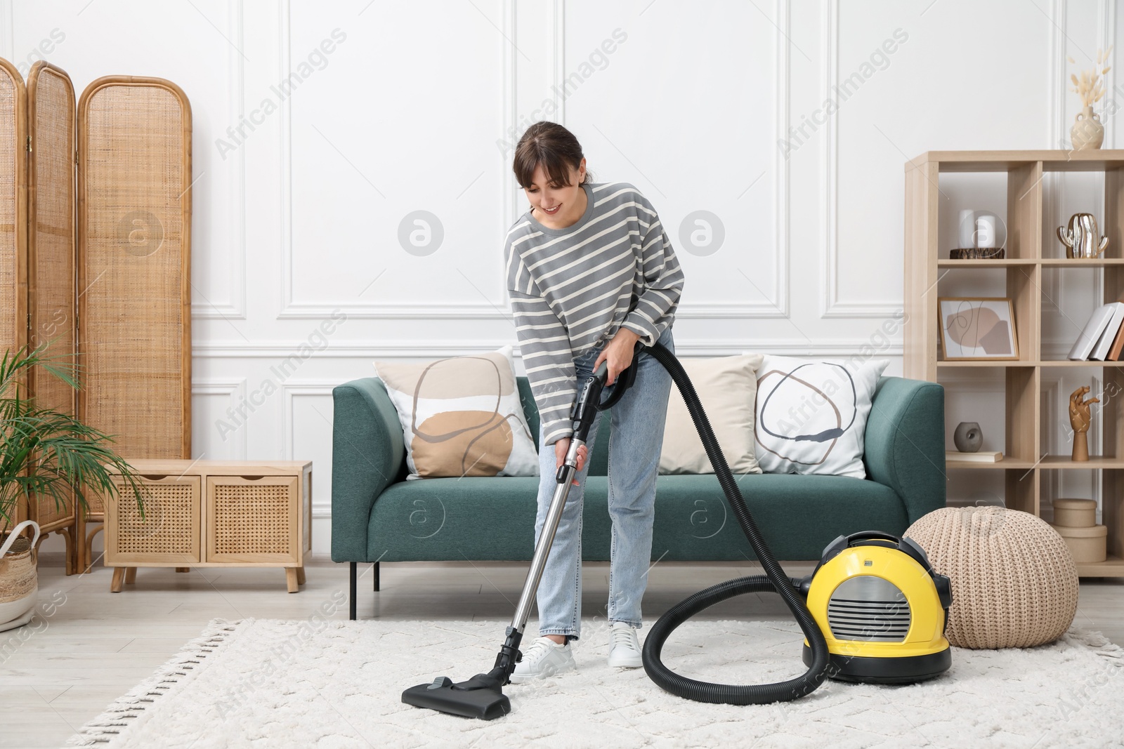 Photo of Young woman cleaning carpet with vacuum in living room