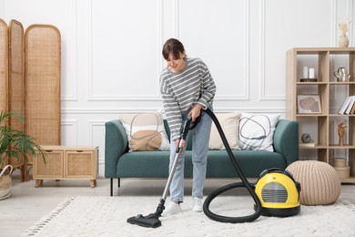 Photo of Young woman cleaning carpet with vacuum in living room