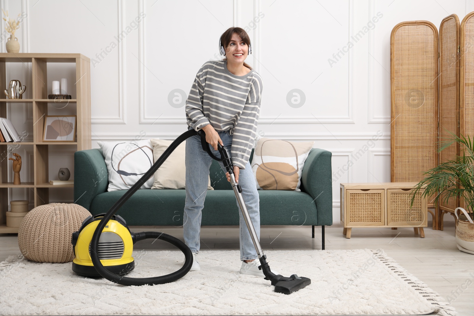 Photo of Young woman wearing headphones cleaning carpet with vacuum in living room