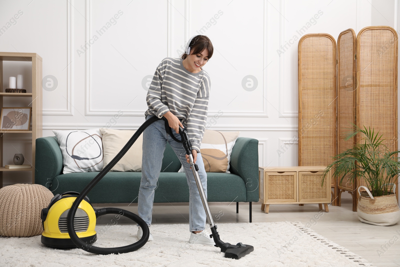 Photo of Young woman wearing headphones cleaning carpet with vacuum in living room