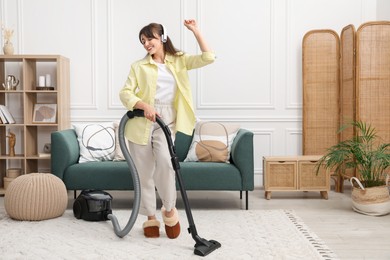 Photo of Young woman with headphones vacuuming carpet in living room