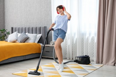 Photo of Young woman with headphones having fun while vacuuming carpet in bedroom