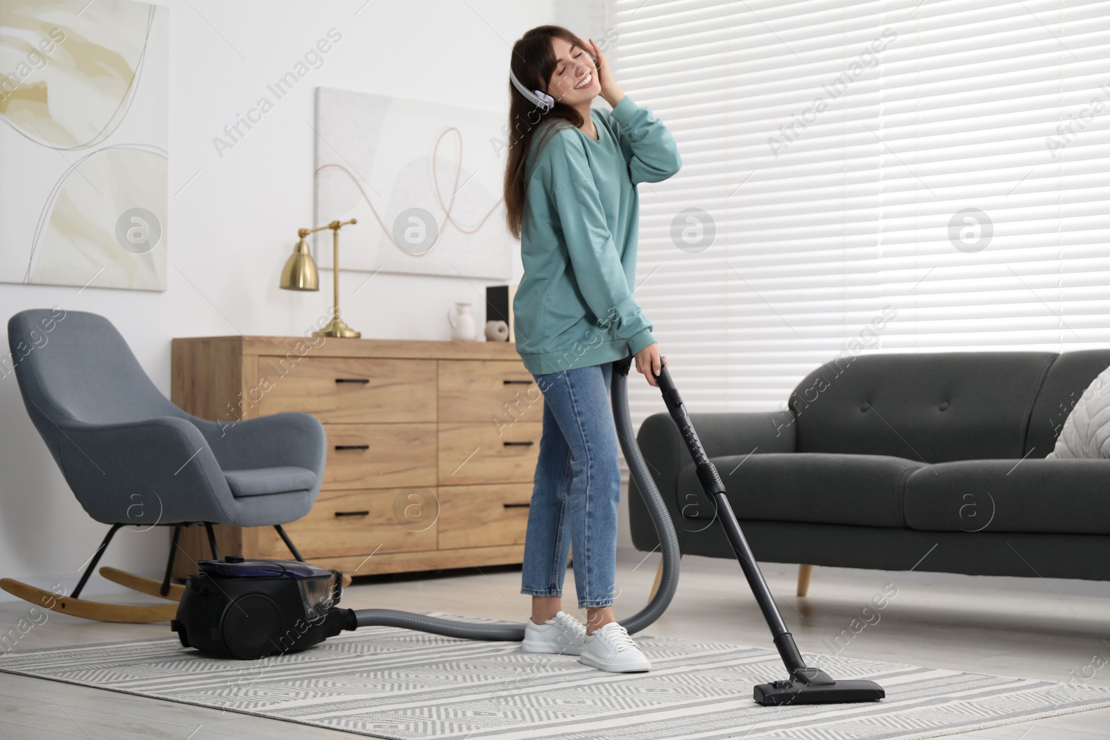 Photo of Young woman in headphones vacuuming carpet at home