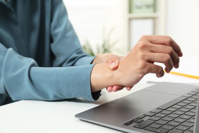 Photo of Carpal tunnel syndrome. Woman suffering from pain in wrist at desk indoors, closeup