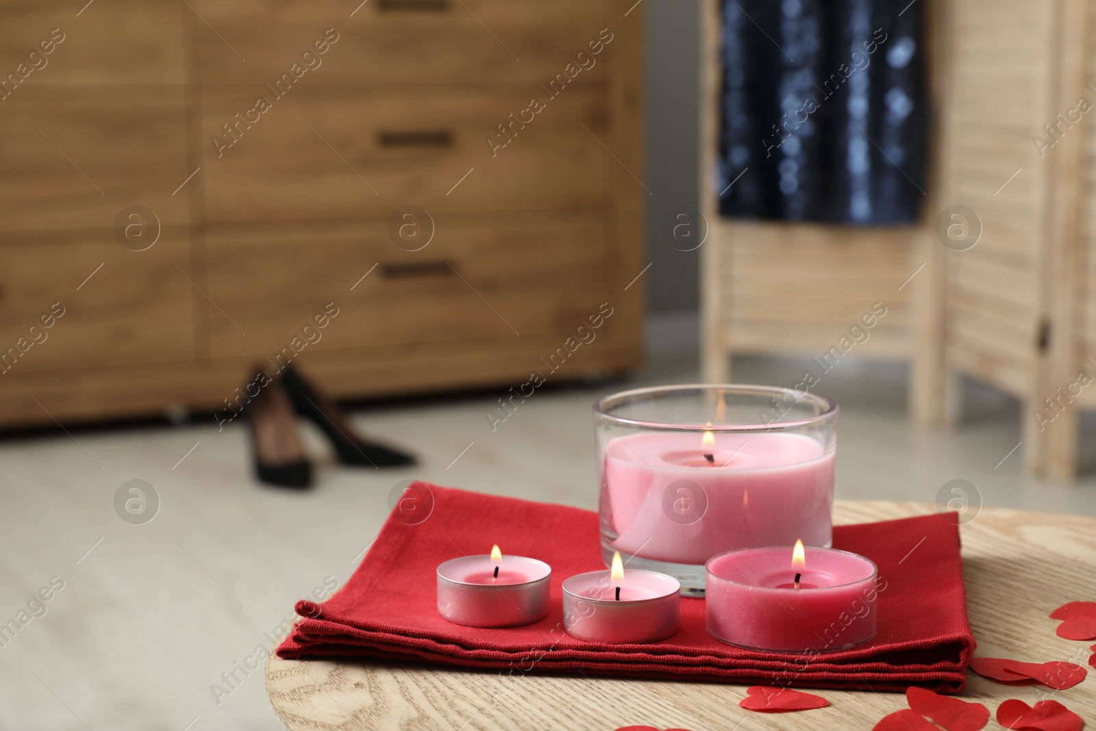 Photo of Burning candles, napkin and decorative hearts on wooden table indoors, closeup. Space for text