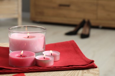 Photo of Burning candles and napkin on wooden table indoors, closeup. Space for text