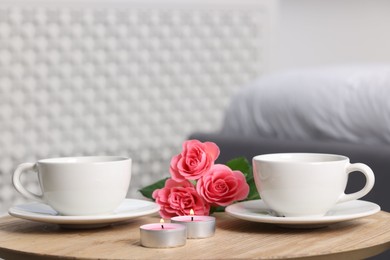 Burning candles, two cups of drink and flowers on wooden table indoors, closeup