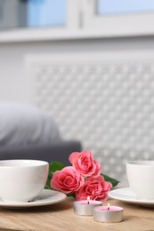 Photo of Burning candles, two cups of drink and flowers on wooden table indoors. Space for text