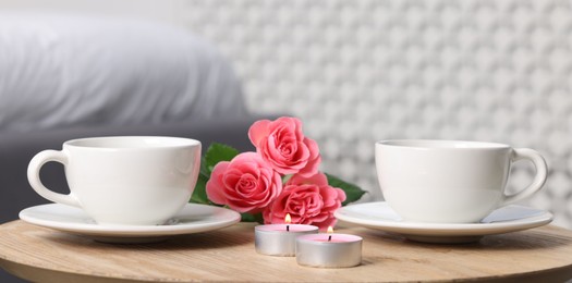 Photo of Burning candles, two cups of drink and flowers on coffee table indoors, closeup