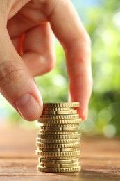 Photo of Woman stacking coins at wooden table, closeup