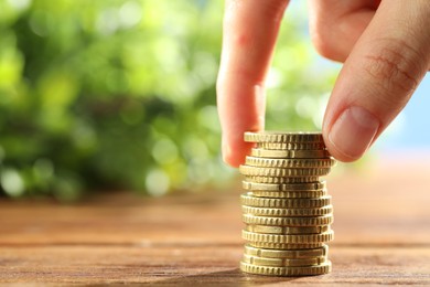 Photo of Woman stacking coins at wooden table, closeup. Space for text