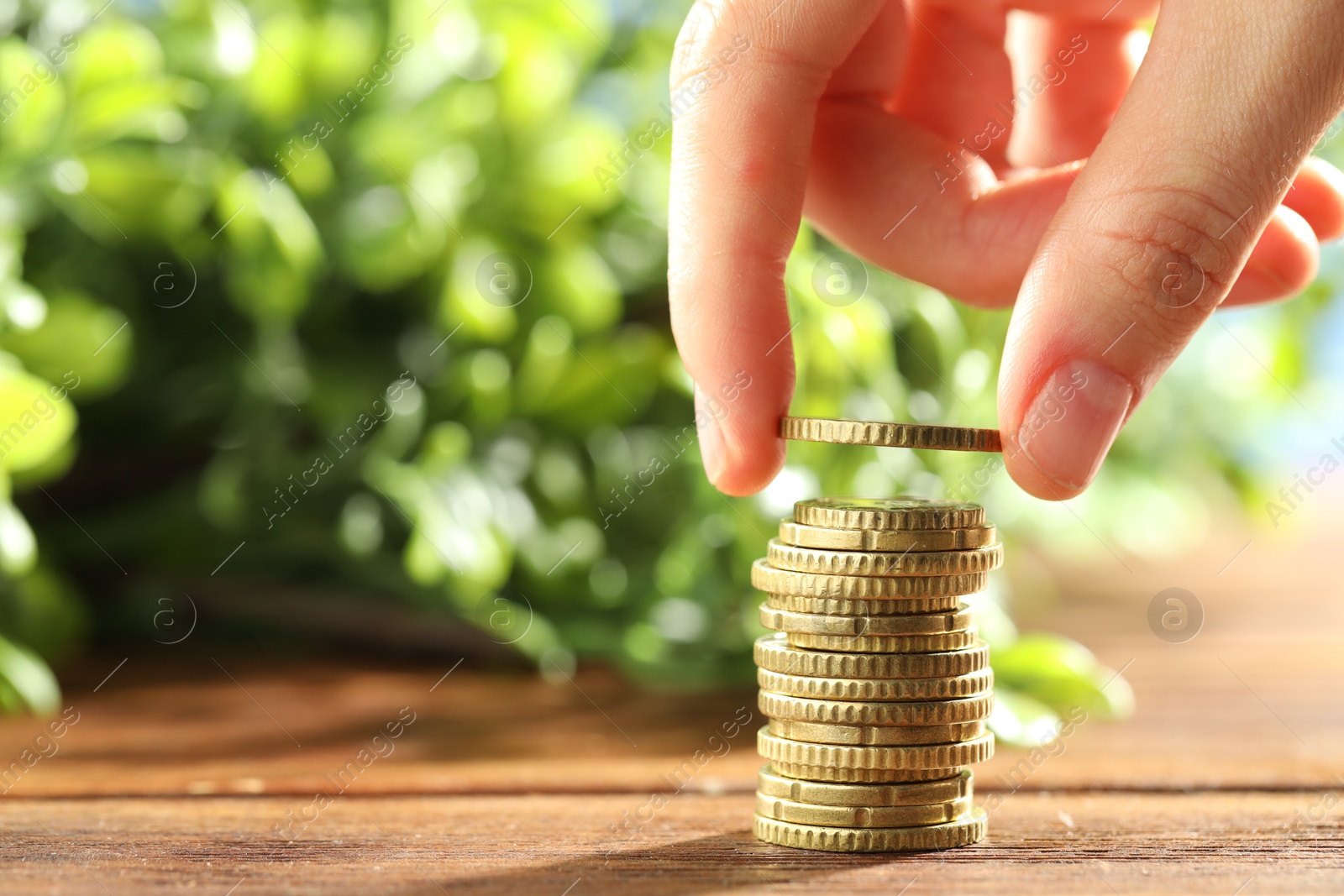 Photo of Woman stacking coins at wooden table, closeup