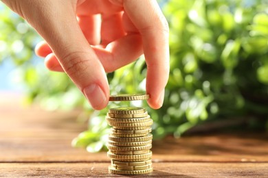 Photo of Woman stacking coins at wooden table, closeup