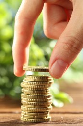 Photo of Woman stacking coins at wooden table, closeup