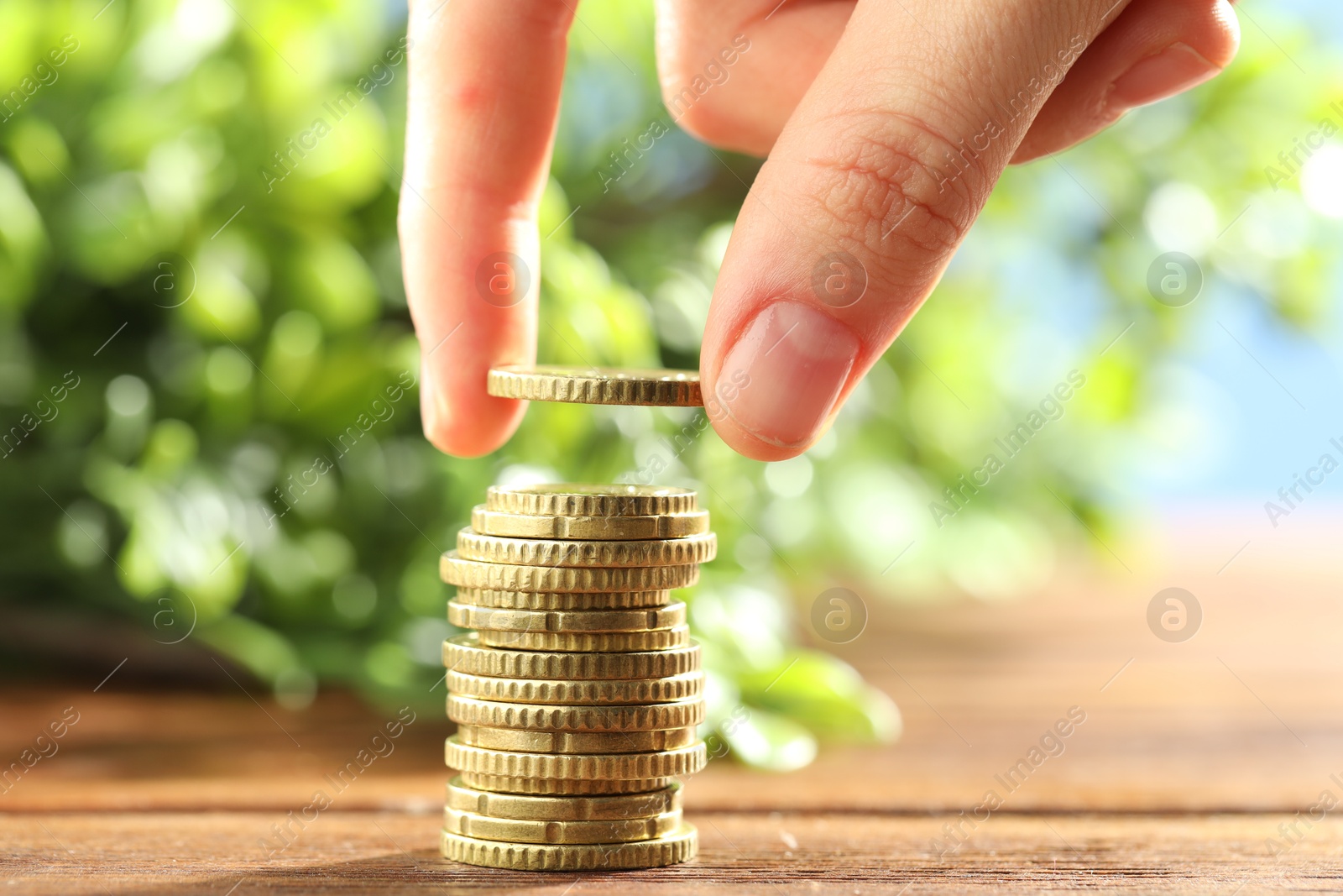 Photo of Woman stacking coins at wooden table, closeup