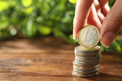 Woman stacking coins at wooden table, closeup. Space for text