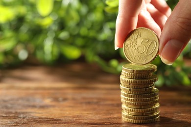 Photo of Woman stacking coins at wooden table, closeup. Space for text