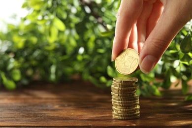 Photo of Woman stacking coins at wooden table, closeup. Space for text