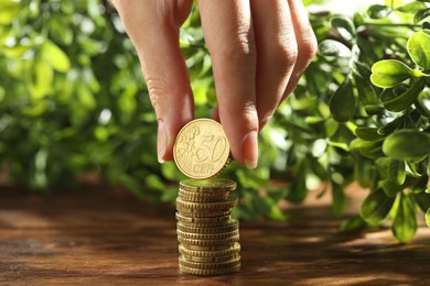 Photo of Woman stacking coins at wooden table, closeup