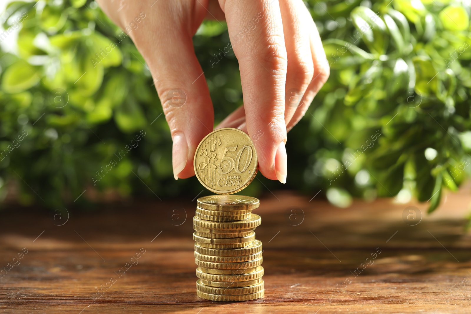 Photo of Woman stacking coins at wooden table, closeup