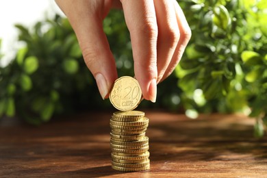 Photo of Woman stacking coins at wooden table, closeup