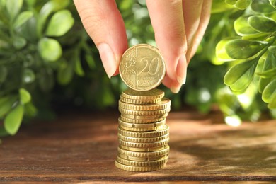 Photo of Woman stacking coins at wooden table, closeup