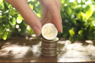 Photo of Woman stacking coins at wooden table, closeup