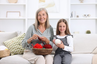 Happy grandmother with granddaughter holding knitting needles and yarn on sofa at home