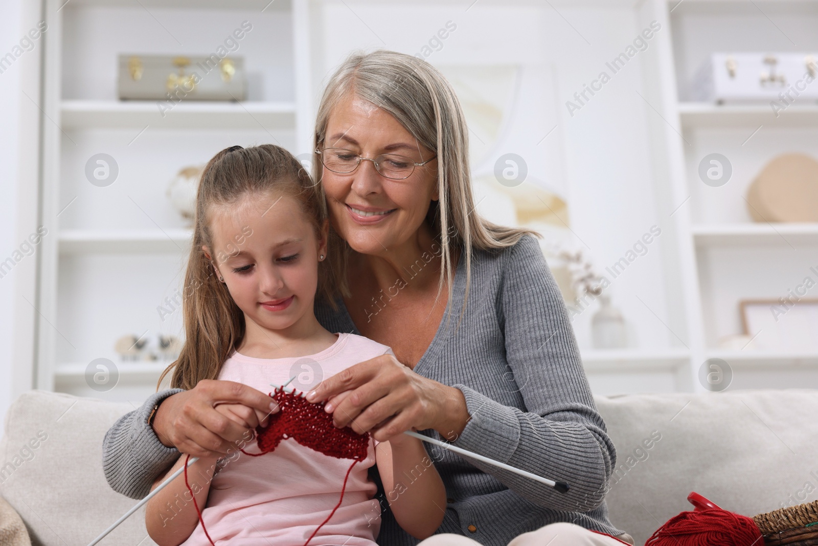 Photo of Smiling grandmother teaching her granddaughter to knit at home